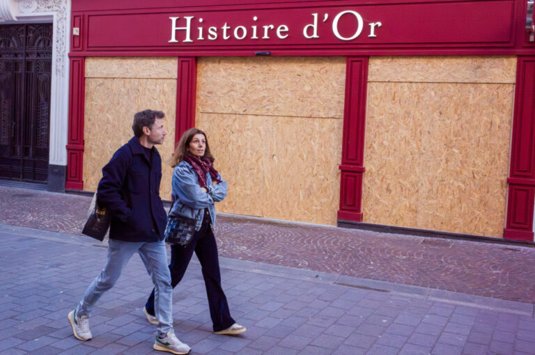 France, Lille, 2026-10-24. Two pedestrians walk past the red Histoire d Or storefront, with wooden panels covering its w