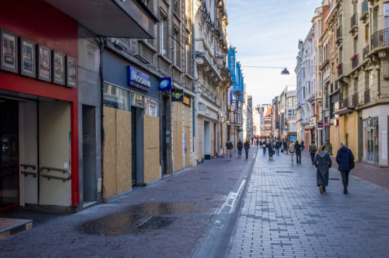 France, Lille, 2026-10-24. Pedestrians walk along a paved shopping street lined with shops whose windows are covered wit