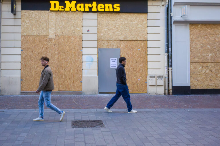 France, Lille, 2026-10-24. Two pedestrians walk in opposite directions past the boarded Dr. Martens storefront and a doo