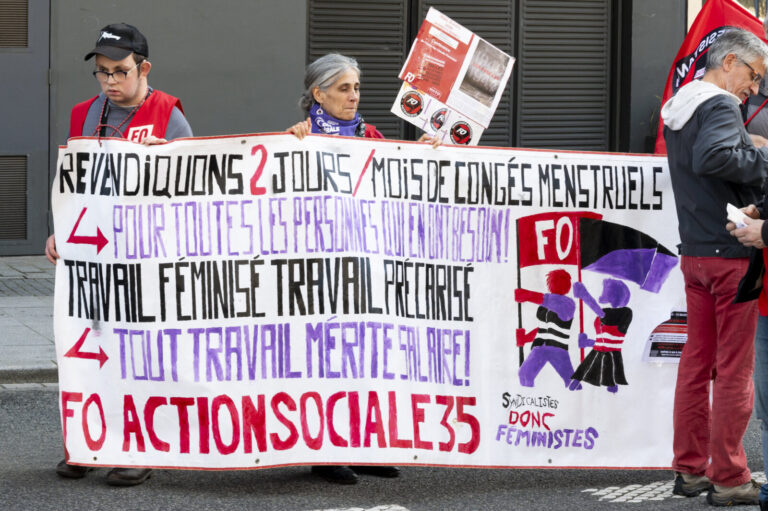 France, Rennes, 2026-03-08. Several protesters stand in the street holding a large banner calling for menstrual leave an