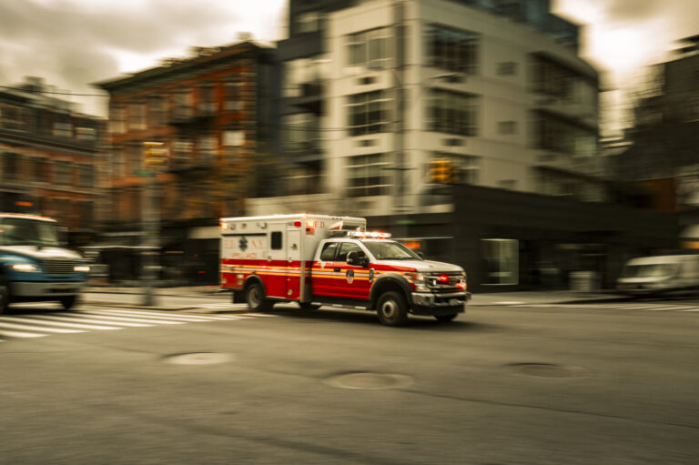 USA, New York, 2024-12-05. A red and white ambulance is captured in motion on a city street in New York. The image shows